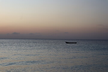 Fototapeta na wymiar Kendwa, Zanzibar Island, Tanzania solo fishing boat against the setting sun and cloudy sky.