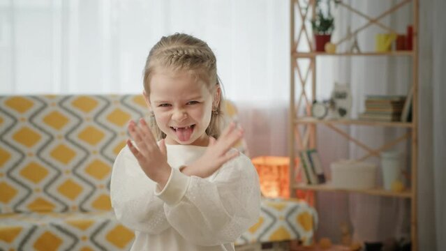 Disgusted girl crossing arms in rejection. Displeased girl shaking hand then crossing arms and showing tongue in aversion in living room at home.