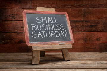Small Business Saturday sign - white chalk handwriting on a blackboard against rustic barn wood -...