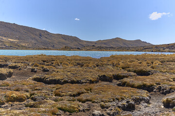 Fototapeta na wymiar Paisaje con suelo erosionado frente a laguna celeste a pies de montañas en un valle con cielo celeste