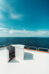 A vertical wide-angle shot of a bright diving safari yacht top deck with a selective focus on the ladder leading downstairs to the middle deck; the ocean and a blue sky in the background