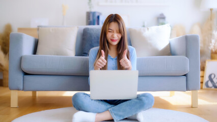 Obraz premium Young asian woman working on her laptop at home, grinning. attractive Asian woman utilizing computer for online schooling, video calling, and conference calls