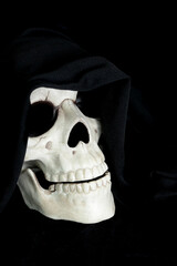 A decorative human skull on a black background. The skull is draped with a black cowl. Copy space