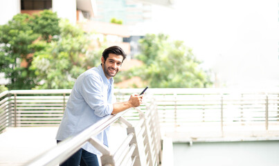 The young man holding  a smartphone to waiting somethig. The man wearing casual cloth at the outside.