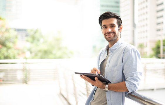 The Young Man Using A Tablet To Working At Out Of Office. The Man Wearing Casual Cloth And Feeling Relaxing And Happy.