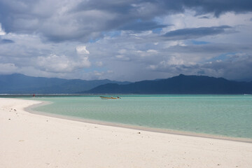 A small motorboat in stunning shallow crystal clear ocean lagoon at sandbar island with mainland of...