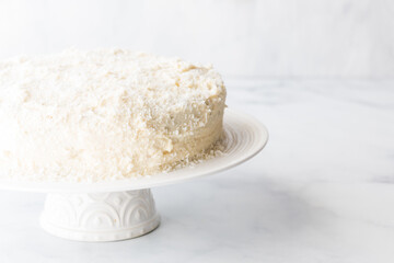 A coconut covered cake brightly lit from the side against a light background.