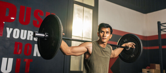 Fototapeta na wymiar Asian sportsman slowly lifting up weight equipment or barbell in gym. 