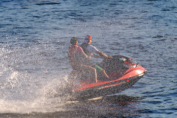 A young man and a girl are sailing on a jet ski in the sea, splashing in different directions....