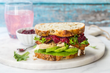 A turkey sandwich with avocado and cranberry sauce on multigrain bread.