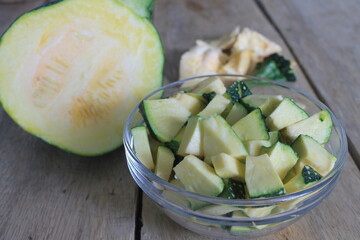 Slices of young green pumpkin in a glass bowl on a wooden table

