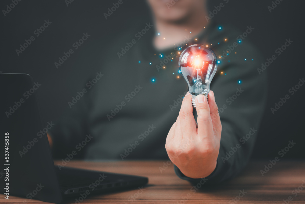Poster man holding a light bulb while working on the computer to think and create new ideas with technologi
