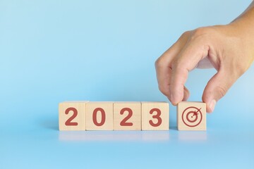 Start New Year 2023 business target goal concept. Human hand stacking wooden blocks with 2023 target icon.