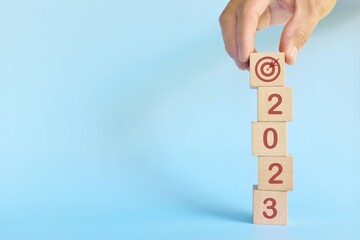 Start New Year 2023 business target goal concept. Human hand stacking wooden blocks with 2023...
