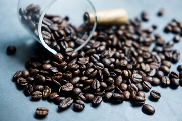 Roasted coffee beans are scattered from glass cup onto a table. Close up