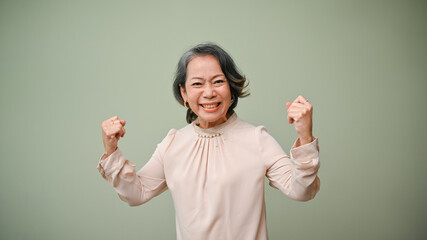 Happy 60s senior Asian woman raising hands, showing strong arms and healthy body