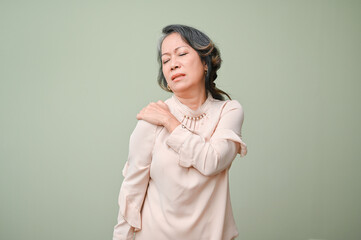 60s aged Asian woman suffering from her shoulder pain, massaging her shoulder