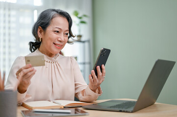 Attractive 60s aged-asian woman using her smartphone to pay her bills on payment application