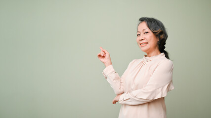 Happy 60s retired asian woman smiling and standing isolated over green studio background.