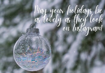 May your holidays be as lovely as they look on Instagram Inspiration joke quote phrase Transparent trendy glass Christmas ball on snowy branch firs in winter forest. Winter holiday background. Happy
