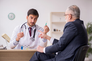 Old businessman visiting young male doctor in vaccination concep