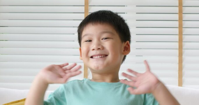 Young little small cute pupil asia people fun waving hand arms raised look at video call webcam camera smile laugh happy face. Health care Gen Z alpha kid baby boy son enjoy play social media at home.