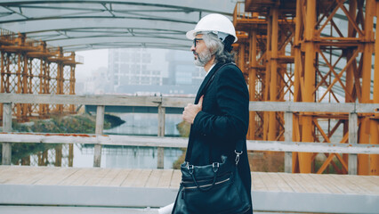 Fototapeta premium Confident mature man investor is working in construction site holding blueprint . People and business concept.