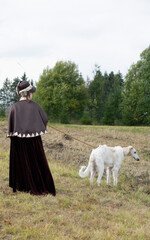 A woman dressed in a historical costume, with an Afghan greyhound.