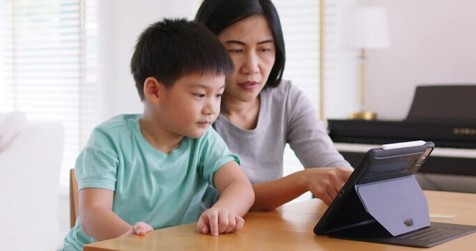 Cute asia people alpha Gen Z kid small boy play video game app online happy mum at home. Enjoy Child care fun class little son and mom study learn upskill idea course on smart digital tablet computer.