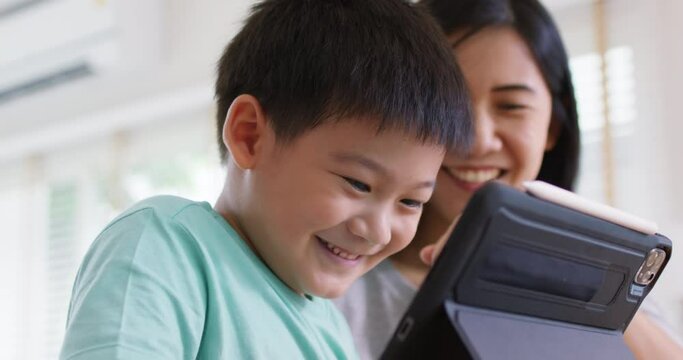 Cute asia people alpha Gen Z kid small boy play video game app online happy mum at home. Enjoy Child care fun class little son and mom study learn upskill idea course on smart digital tablet computer.