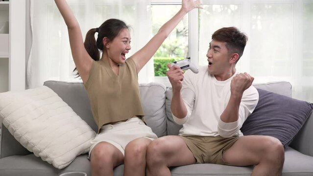 Young Asian couple playing video games on a couch and having fun at home.