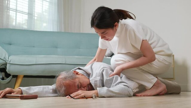 Asian elderly old man with walking stick fall on ground and granddaughter camp to help to support at home in living room, young woman halping her grandfather after falling down on floor, dizziness