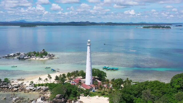 wide aerial of white lighthouse on lengkuas island with belitung on horizon