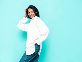 Portrait of young beautiful black woman. Smiling model dressed in summer jeans clothes. Sexy carefree female posing near blue wall in studio. Tanned and cheerful