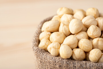 Small linen bag of peeled hazelnuts on wooden background. Tasty white hazelnuts, copy space