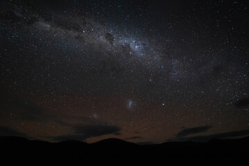 Silhouette of mountains with the beautiful Milky Way above, in the background you can see a dark starry sky with some faint clouds, constellations and stars shining bright.