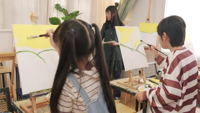 A group of Asian children concentrates on acrylic color picture painting on canvas by brush in an art classroom and creatively learns with talents and skill at the elementary school studio education.