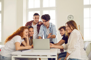 Team of happy college or university students searching for information on laptop computer while...