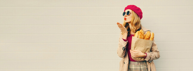 Portrait of beautiful young woman blowing her red lips sending sweet air kiss holding grocery...