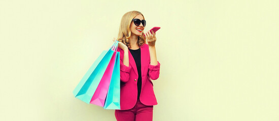 Portrait of beautiful smiling young woman calling on smartphone with shopping bags wearing business...