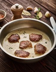 Pork meat medallions with cream sauce in skillet