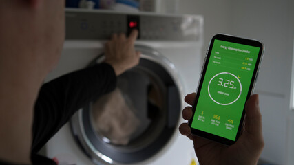 A man holds a smart phone with energy consumption app displaying energy usage in a laundry setting