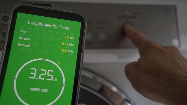 A man holds a smart phone with energy consumption app displaying energy usage in a laundry setting