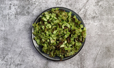 Lettuce and cucumber salad on a round plate on a dark gray background. Top view, flat lay.