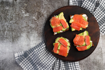 Homemade Salmon avocado sandwiches with cottage cheese on a round wooden cutting board on a dark grey background. Top view, flat lay