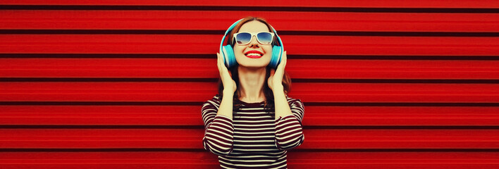 Portrait of happy smiling young woman with headphones listening to music on red background