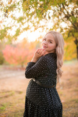 Beautiful young pregnant woman with long blond hair in autumn park in sunny weather. Health and Motherhood.
