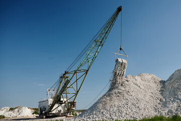 Dragline pours chalk out of bucket at pit against clear sky