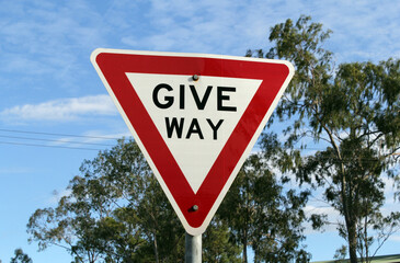 Give way road sign with a tree and the sky in the background