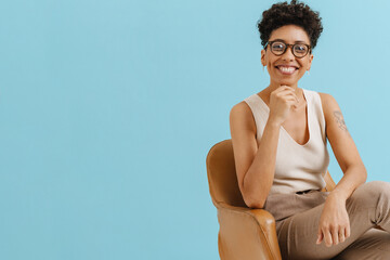 Young curly woman in eyeglasses smiling while sitting on armchair